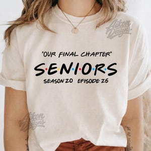May include: Cream-colored t-shirt with the text "OUR FINAL CHAPTER" above "SENIORS" in a colorful, stylized font. Below, it reads "SEASON 20 EPISODE 26". The shirt has rolled-up sleeves.