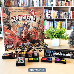 Può includere: Una scatola del gioco da tavolo Zombicide 2nd Edition con personaggi illustrati che combattono contro gli zombi, accompagnata da miniature, organizzatori di componenti in plastica nera e un vassoio nero con il logo Zombicide stampato.