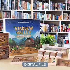 Könnte beinhalten: Ein Stardew Valley Brettspiel-Set mit einer großen quadratischen Spielschachtel mit Bauernhof-Illustration, zwei hölzernen Aufbewahrungsboxen mit lasergeschnittenen Gittermustern, Kartenhaltern und Spielmarken. Der Text lautet Stardew Valley.