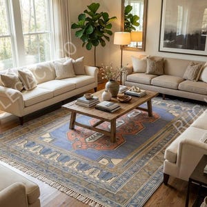 Op de afbeelding: Een woonkamer met drie beige banken rond een groot blauw en oranje patroon tapijt. In het midden staat een houten salontafel en de kamer is ingericht met planten en kunstwerken.