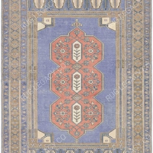 Op de afbeelding: Een rechthoekig vloerkleed in vintage-stijl met een centraal ontwerp in koraal en wit, tegen een lichtblauwe achtergrond. Het vloerkleed heeft bloemen- en geometrische patronen, omlijst door een rand van complementaire kleuren en ontwerpen.