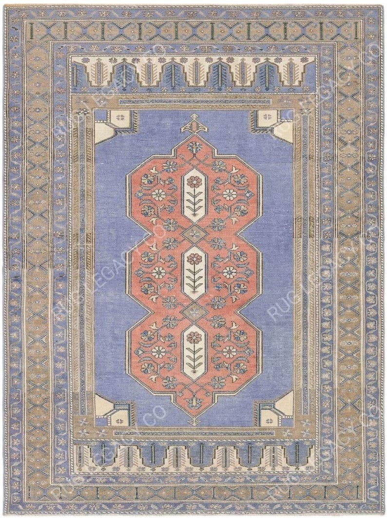 Op de afbeelding: Een rechthoekig vloerkleed in vintage-stijl met een centraal ontwerp in koraal en wit, tegen een lichtblauwe achtergrond. Het vloerkleed heeft bloemen- en geometrische patronen, omlijst door een rand van complementaire kleuren en ontwerpen.
