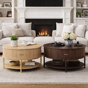 May include: Two round coffee tables with ribbed sides and lower shelves. One is light wood with gold legs, the other is dark wood with black legs. A white sofa and fireplace are in the background, creating a cozy living room setting.