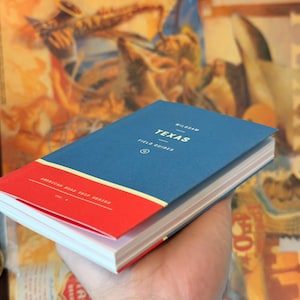 May include: A blue and red book titled "Texas Field Guides" from the American Road Trip Series. The book is held in a hand, with a vintage-style poster in the background. The book's cover has the word "Texas" in white.