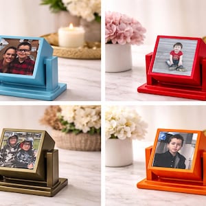 Könnte beinhalten: Vier drehbare Bilderrahmen in verschiedenen Farben: Hellblau, Rot, Bronze und Orange. Jeder Rahmen zeigt ein Foto. Die Rahmen stehen auf einer weißen Oberfläche, mit Kerzen und Blumen im Hintergrund.