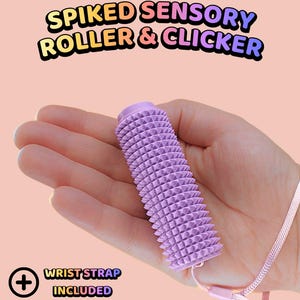 May include: A lavender cylindrical sensory roller with a spiked texture, featuring a matching light purple wrist strap attached to one end. The text SPIKED SENSORY ROLLER & CLICKER is displayed at the top, with WRIST STRAP INCLUDED listed below.