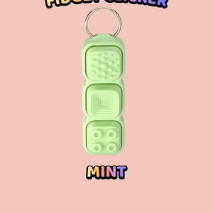 Może przedstawiać: Miętowy fidget clicker z metalowym k&oacute;łkiem. Urządzenie posiada trzy ułożone w stos przyciski o r&oacute;żnych fakturach: kropkowaną powierzchnię, wz&oacute;r kwadratu w kwadracie oraz cztery wypukłe k&oacute;łka. Tekst: TEXTURED BUTTON FIDGET CLICKER MINT.