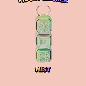 Może przedstawiać: Pastelowy brelok typu fidget clicker z trzema kwadratowymi przyciskami o r&oacute;żnych wypukłych fakturach, w tym kropkami, koncentrycznymi kwadratami i czterema okręgami. Widoczny jest tekst "TEXTURED BUTTON FIDGET CLICKER" oraz "MIST" w kolorowych literach.