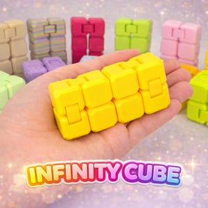 May include: A yellow Infinity Cube is held in a hand, with several other colourful cubes in the background. The cubes are in various colours, including blue, pink, green, and beige. The text "INFINITY CUBE" is displayed in a colourful font.