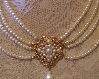 Op de afbeelding: Een meerstrengs parelketting met een gouden hanger met een bloemmotief en een enkele parel.