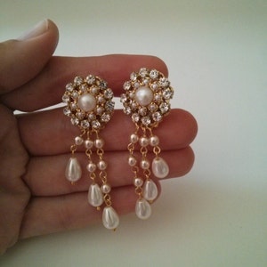 May include: Gold tone earrings with a cluster of clear rhinestones and a single pearl in the center. The earrings have a dangling chain with multiple pearls.