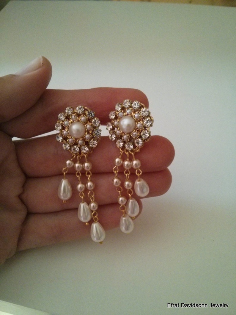 May include: Gold tone earrings with a cluster of clear rhinestones and a single pearl in the center. The earrings have a dangling chain with multiple pearls.