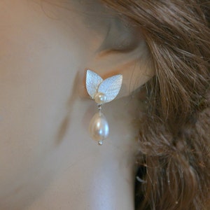 May include: Silver leaf earrings with a single pearl drop. The leaves are textured and the pearl is white.