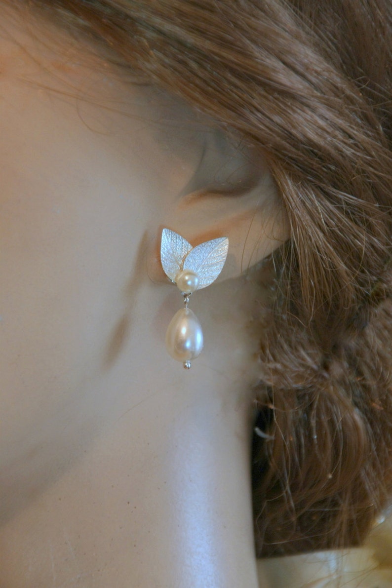 May include: Silver leaf earrings with a single pearl drop. The leaves are textured and the pearl is white.