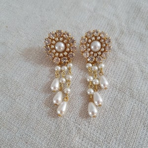 May include: A pair of gold earrings with a round, crystal-encrusted design and a dangling pearl drop.