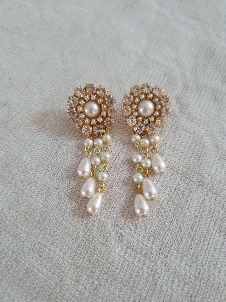 May include: A pair of gold earrings with a round, crystal-encrusted design and a dangling pearl drop.