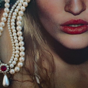 May include: A multi-strand pearl necklace with a red gemstone pendant. The necklace is made of white pearls and has a classic design.