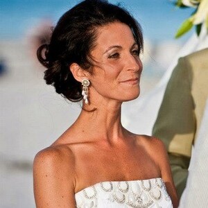 May include: A bride wearing a white strapless wedding dress with beaded embellishments. The dress has a fitted bodice and a flowing skirt. The bride is smiling and looking to the side.