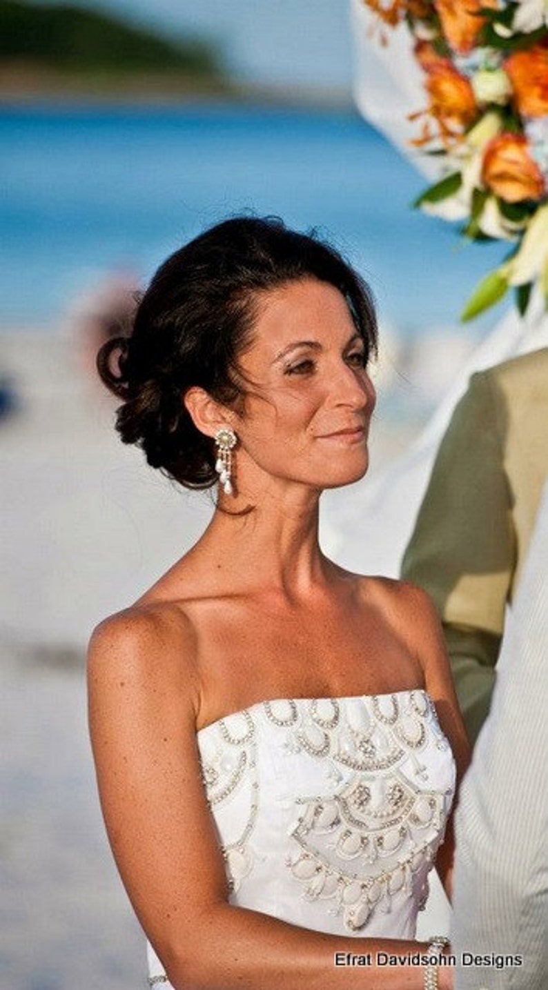 May include: A bride wearing a white strapless wedding dress with beaded embellishments. The dress has a fitted bodice and a flowing skirt. The bride is smiling and looking to the side.