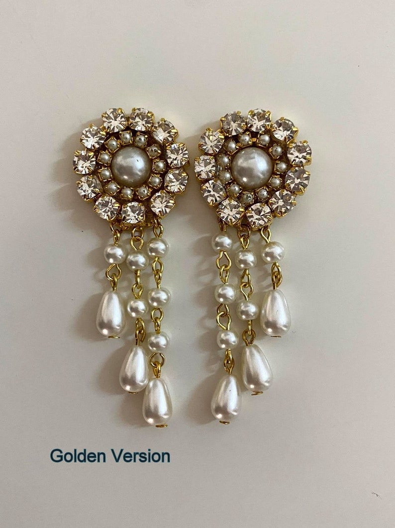 May include: Gold tone earrings with a large pearl and crystal cluster at the top and a dangling chain of pearls. The earrings are labeled "Golden Version".