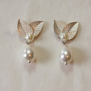 May include: A pair of silver leaf earrings with a pearl drop. The leaves are textured and the pearls are white.