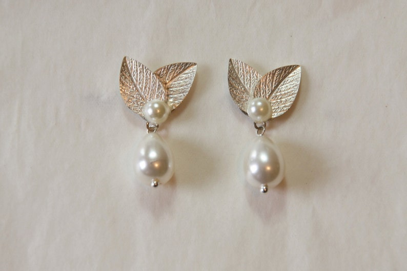 May include: A pair of silver leaf earrings with a pearl drop. The leaves are textured and the pearls are white.