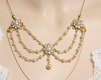 Op de afbeelding: Een gouden ketting met drie rijen nepparels en drie bloemvormige hangers met strass. De ketting heeft een enkele parel hanger.