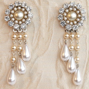 May include: A pair of dangle earrings with a large, round, crystal-encrusted centerpiece and a drop of pearls.
