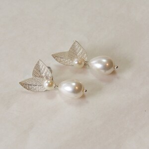 May include: A pair of silver earrings with a leaf design and a white pearl drop.