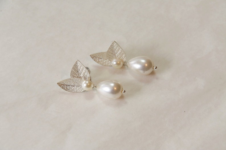 May include: A pair of silver earrings with a leaf design and a white pearl drop.