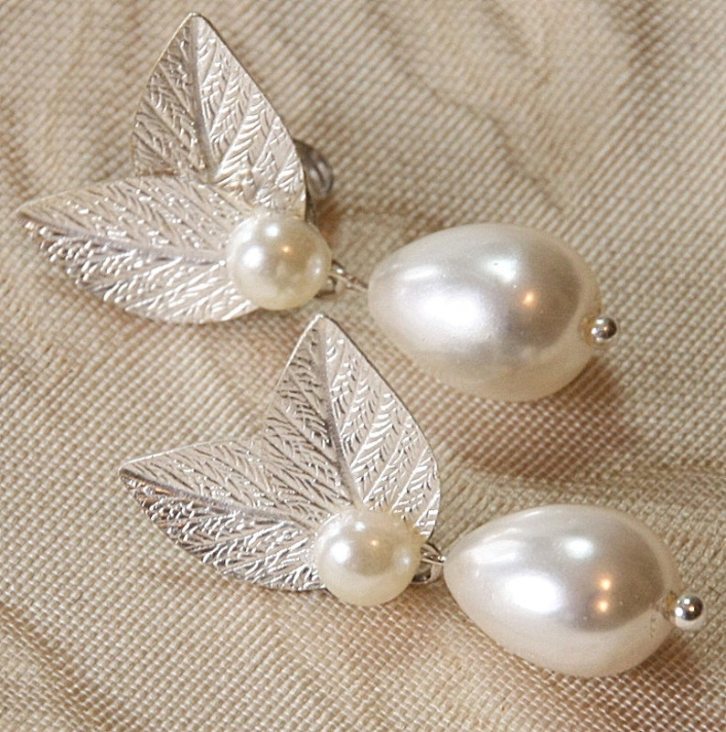 May include: A pair of silver leaf earrings with a pearl drop on each earring.