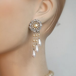 May include: A pair of dangle earrings with a round, crystal-encrusted center and a pearl drop. The earrings feature three pearl drops hanging from the center.