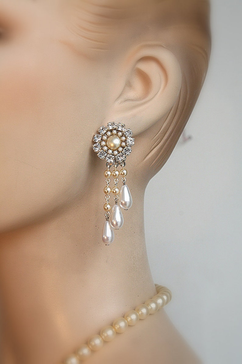 May include: A pair of dangle earrings with a round, crystal-encrusted center and a pearl drop. The earrings feature three pearl drops hanging from the center.