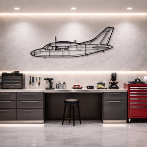 May include: Black metal airplane wall art. The airplane is a side profile with detailed lines, mounted on a light-colored wall. The art piece is above a workbench with tools and a stool.