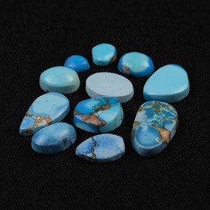 Pode incluir: Uma coleção de nove cabochões de turquesa em várias formas e tamanhos, que vão do azul claro ao azul escuro, com alguns mostrando veios marrons. As pedras estão dispostas em um padrão circular sobre um fundo preto.