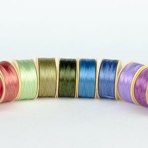 May include: A set of ten spools of thread in various colors, including red, green, blue, and purple. The spools are arranged in a semi-circle.