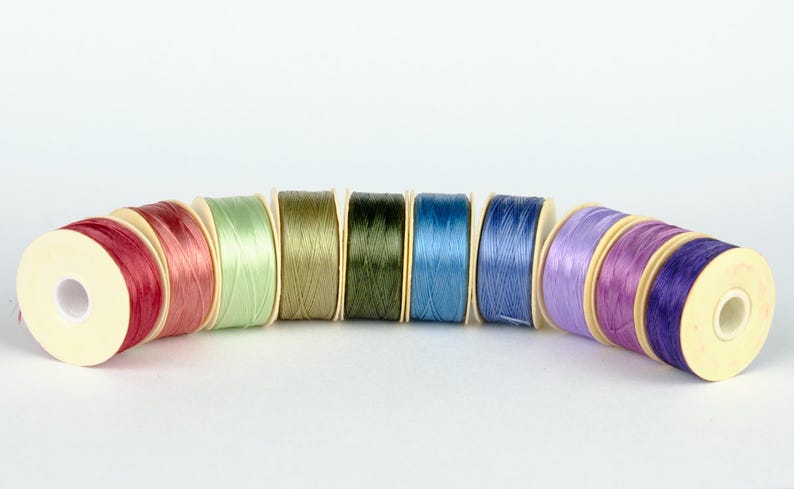 May include: A set of ten spools of thread in various colors, including red, green, blue, and purple. The spools are arranged in a semi-circle.