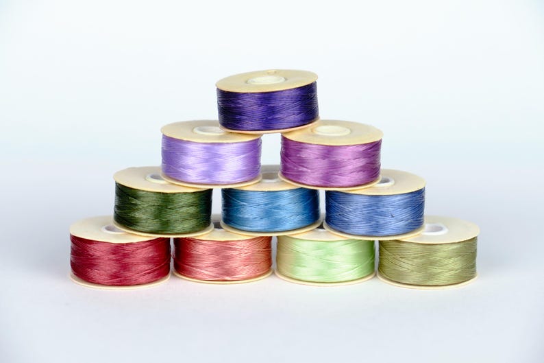 May include: A collection of ten spools of thread in various colors, including purple, blue, green, and red. The spools are arranged in a pyramid shape.