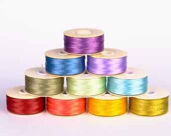 May include: A pyramid of colorful thread spools in shades of red, orange, yellow, green, blue, and purple. The spools are arranged on a white background, showcasing the vibrant colors of the thread. Ideal for sewing and crafting projects.