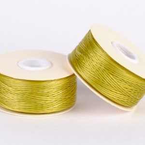 May include: Two spools of yellow waxed thread on white cardboard spools.
