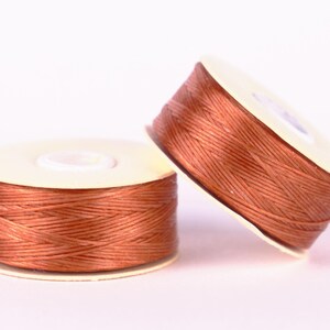 May include: Two spools of brown thread wound on white plastic bobbins.