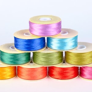 May include: A pyramid of colorful thread spools. The spools are arranged in a neat stack, showcasing a variety of vibrant colors including pink, red, orange, yellow, green, blue, and purple. Each spool is filled with thread.