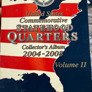 Pode incluir: Um álbum de coleção retangular para United States Commemorative Statehood Quarters 2004-2008 Volume II. A capa apresenta um mapa dos Estados Unidos com listras vermelhas e brancas e uma seção azul escura, com texto sobre a coleção.