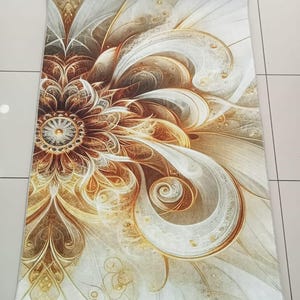 May include: A rectangular rug with a floral design. The rug features a large, stylized flower in shades of brown, gold, and white. The design has intricate details and a swirling, abstract pattern. The rug is placed on a tiled floor.