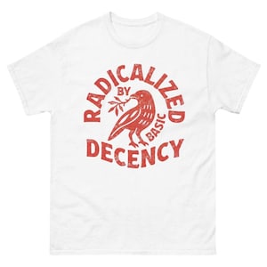 Puede incluir: Camiseta blanca con un gráfico rojo. El gráfico presenta un pájaro sosteniendo una rama, rodeado por las palabras "RADICALIZED BY BASIC DECENCY" en una disposición circular. La camiseta tiene mangas cortas y cuello redondo.
