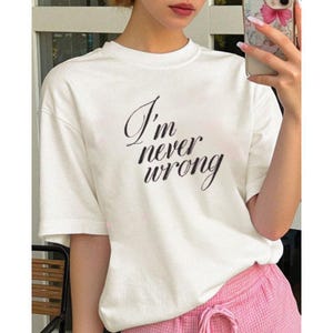 Peut inclure: T-shirt blanc à manches courtes avec l'inscription noire "I'm never wrong". Le t-shirt a un col rond et une coupe ample. Le modèle porte un short rose.