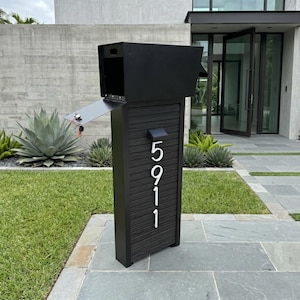 May include: A freestanding black post box with a horizontal slatted front panel featuring the vertical white house numbers 5911. The unit includes a top-loading compartment with an open hinged door and a small solar light fixture above the numbers.