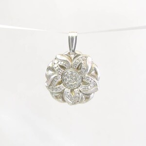 Puede incluir: Un colgante de plata en forma de flor con un centro de peque&ntilde;as piedras transparentes.