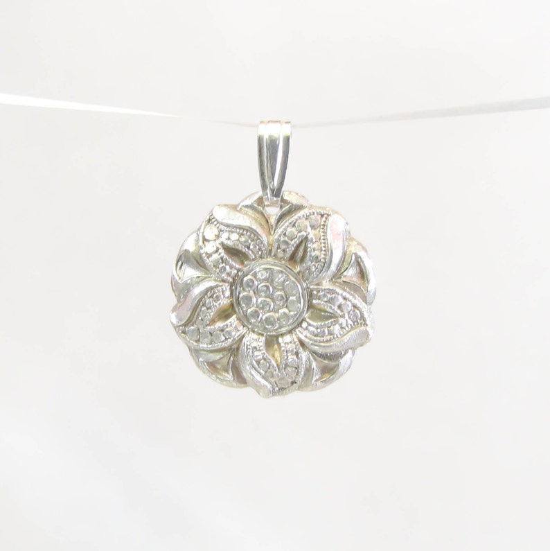 Puede incluir: Un colgante de plata en forma de flor con un centro de peque&ntilde;as piedras transparentes.