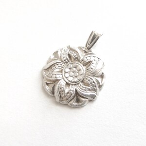 Puede incluir: Un colgante de plata en forma de flor con un dise&ntilde;o detallado. El colgante tiene una forma circular con un dise&ntilde;o de flor de cinco puntas en el centro.